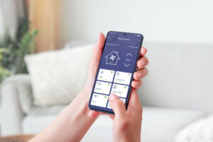 Woman’s hand holding a mobile phone, showcasing a smart home app. Smart living concept. Decorated living room in background