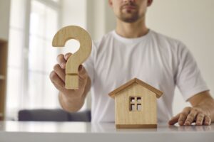 Confusion young man who is hesitant about buying his home shows wooden question mark.